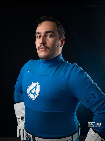 Cosplay Mr Fantastique (Marvel), combinaison bleue au « 4 » et moustache, fond bleu — Fabrice Fiorucci Photographe